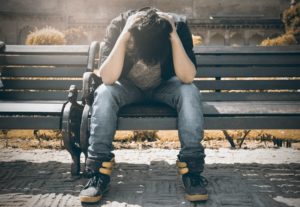 A man sitting on a park bench, head in hands, struggling with his thoughts, possibly about minor attraction.