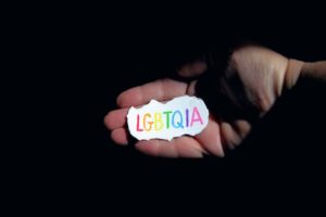 Hand holding a piece of paper with LGBTQIA written on it in rainbow.