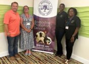 Justin Moyer and Dr. Jennifer Weeks on the left of a banner with details on the summit and Angela Dixon and Denise Agard from the Barbados Probation Department on the right.