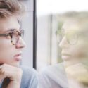 A man wearing glasses looks out a window.
