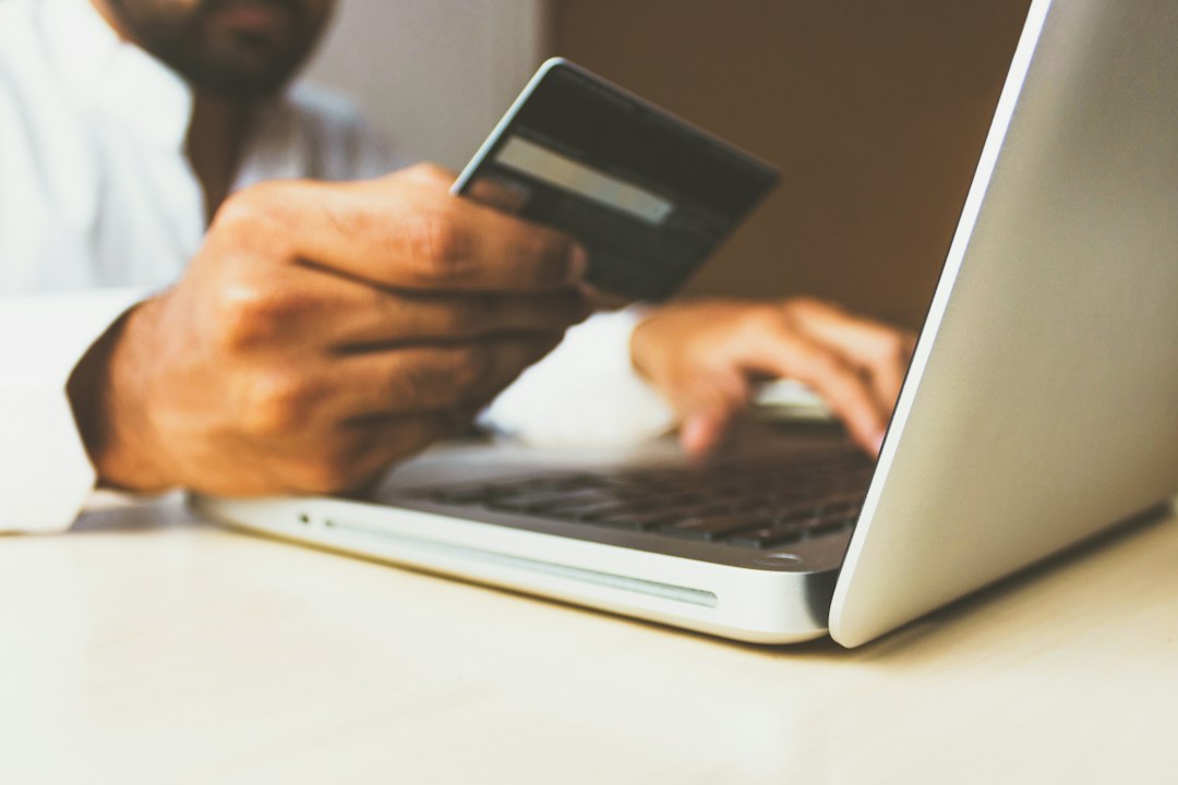 Person holding a payment card beside a laptop, illustrating the Shopify checkout upgrade.